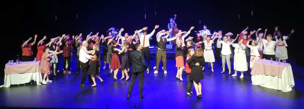 Chorale habillée de noir, blanc et rouge, avec des couples qui dansent devant